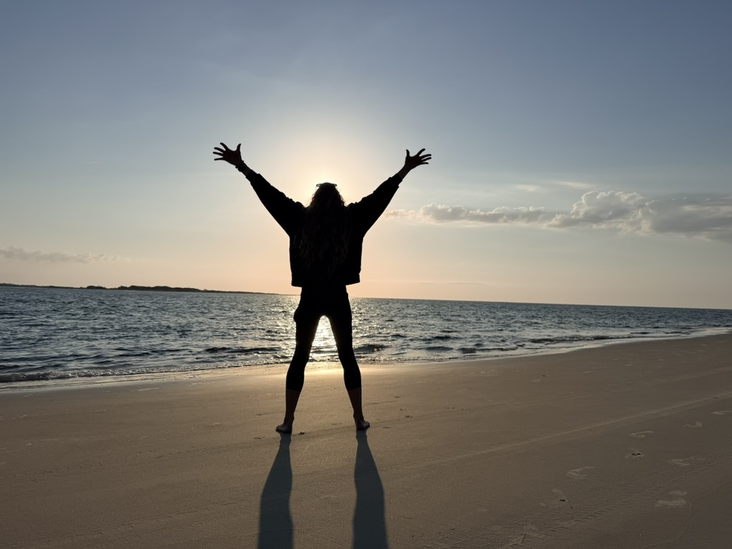 Jena silhouetted on the beach at sunrise, arms raised